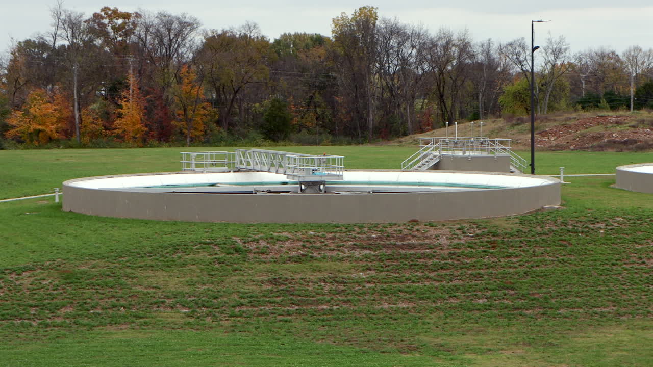 Clarifier pools at a wastewater treatment plant slowly rotate and settle, captured in a smooth left-to-right pan, revealing the industrial water treatment process