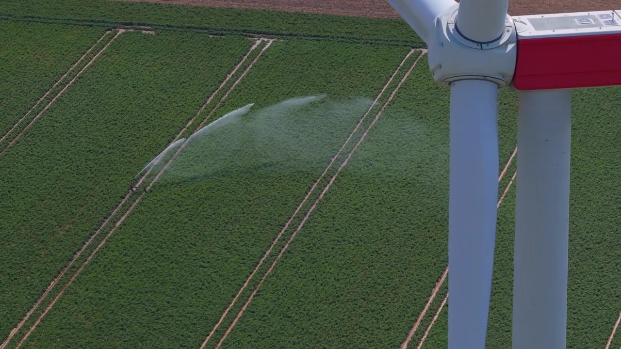 Impressionante ripresa aerea che rivela un sistema di irrigazione agricolo che irriga le colture, con una grande pala di turbina eolica in primo piano