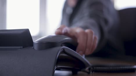 close-up shot of a person placing a phone receiver on a desk, focus on office setting