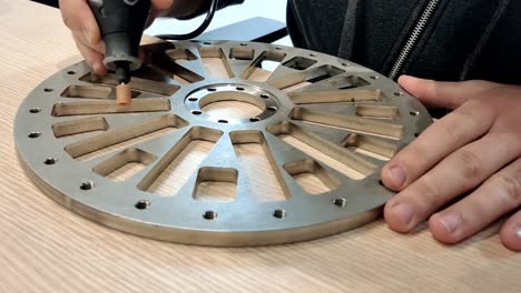 Close-up-of-mechanic-man's-hand-performing-sanding-smoothing-on-metal-part-with-machine-on-the-wooden-table-surface