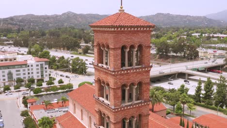 close up drone aerial footage, of st andrew catholic church clock bells tower landmark of pasadena city california with freeway traffic in the background on a cloudy afternoon day