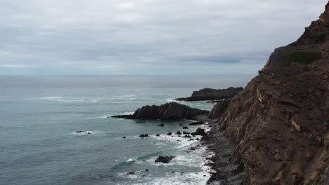 rugged coastline of praia da arrifana in west portugal on overcast day, aerial flyover view