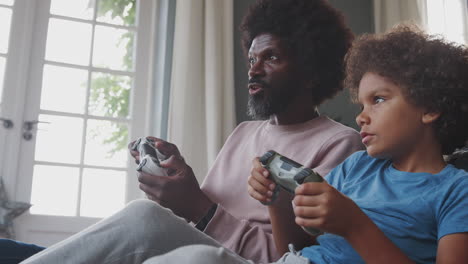 happy middle aged black father and his pre teen son sitting on the floor in their living room talking and playing video games together, close up