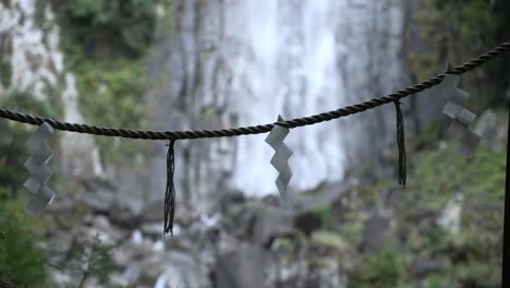 close up of shide papers hanging on rope in front of nachi falls in nachikatsuura, japan