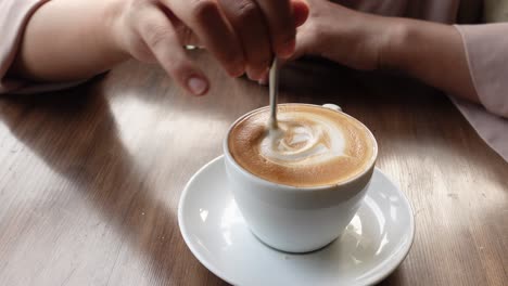 woman stirring a latte with latte art in a coffee shop