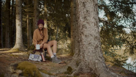 female explorer sitting with coffee mug on tree stump