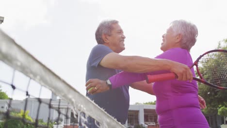 Video-of-happy-biracial-senior-couple-embracing-on-tennis-court