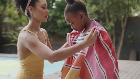 african american mother and daughter covering with towel by swimming pool in garden, slow motion