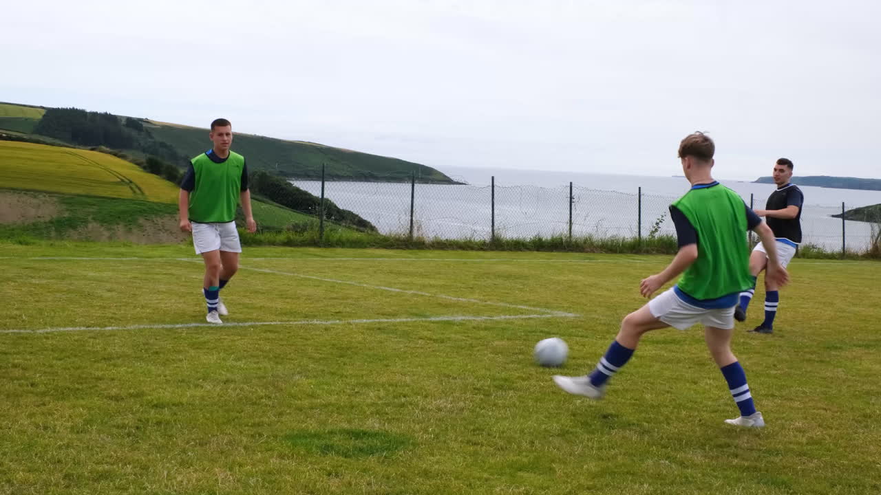 Players practicing soccer on grassy field by sea, wearing green jerseys
