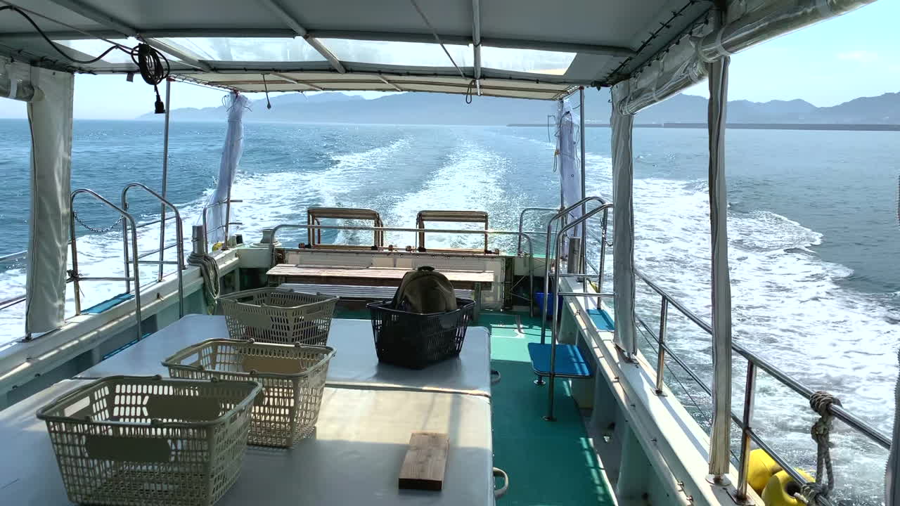 Rear view of a speedboat sailing in the ocean leaving a trail of white foam as it moves away from the coast with a majestic mountain in the background and a beautiful blue sky in daylight