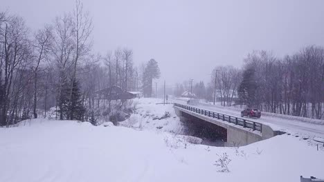 slow motion aerial shot of an suv following a truck with a snowmobile trailer over a bridge in a snow storm