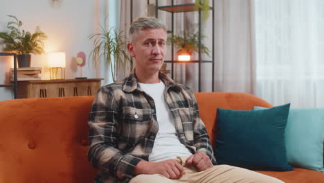 mature man denying or saying no with finger gesture on couch at home