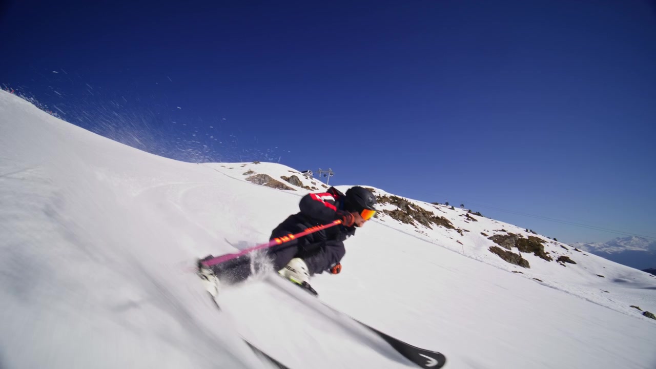 Sciatore che intaglia piste battute ad alta velocità a Nendaz, parte del comprensorio sciistico 4 Vallées nelle Alpi svizzere. Sci alpino d'élite con potenti spruzzi di neve e tecnica di precisione.