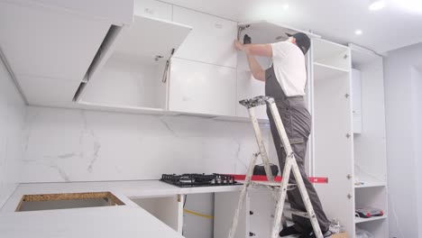 a young man is holding a kitchen cabinet door and a cordless screwdriver