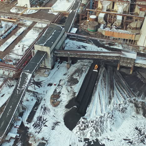yellow excavator smoothes black ash from coal under the bridge in the territory of the heating power station. aerial view.