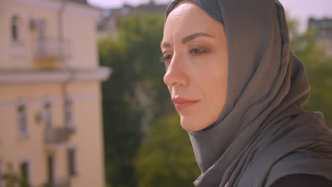 closeup portrait of young attractive muslim woman in hijab looking at landscape and turning to camera standing on balcony of the house