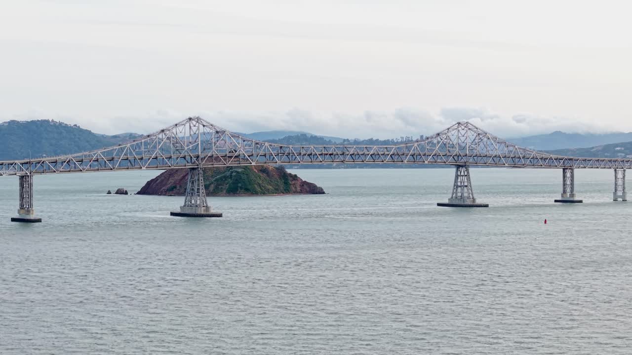 The Richmond–San Rafael Bridge spans across the glistening water, seen from above as traffic flows steadily and the horizon glows in soft afternoon hues. Filmed in 4K as the camera slowly zooms in.