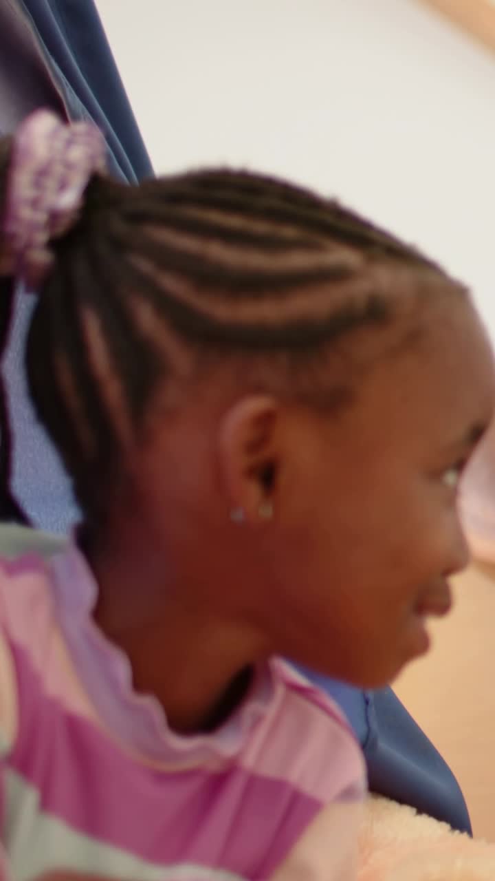 Girl on bed turning right, smiling and leaning forward after off-camera call for kids media, braids