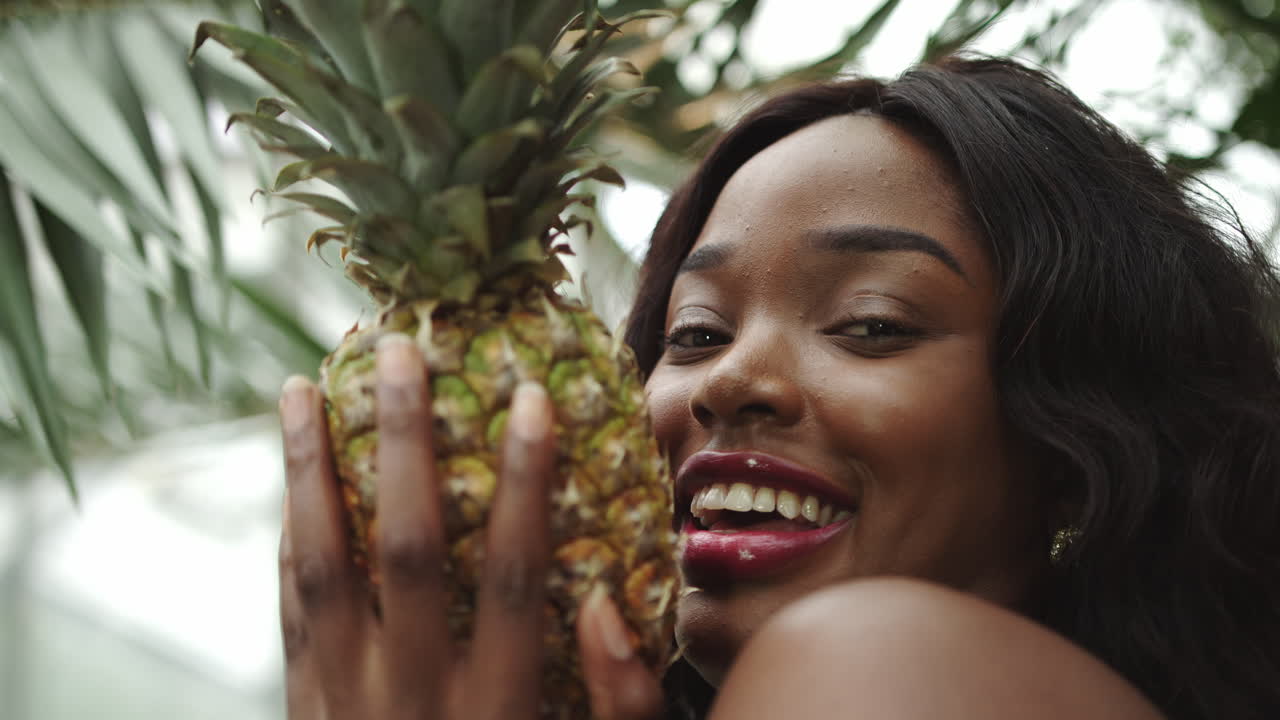 Shooting close up young beautiful african american girl holding a pineapple and smiling at the