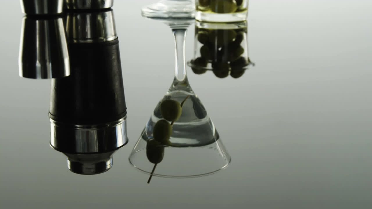 Carta grigia che brucia sopra attrezzatura da barman e olive in un bicchiere da cocktail su sfondo grigio