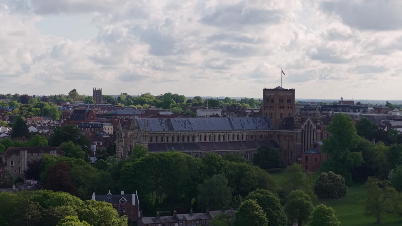 A cinematic drone shot of St Albans Cathedral on a cloudy day, capturing the dramatic landscape, gothic architecture, and surrounding scenery from above