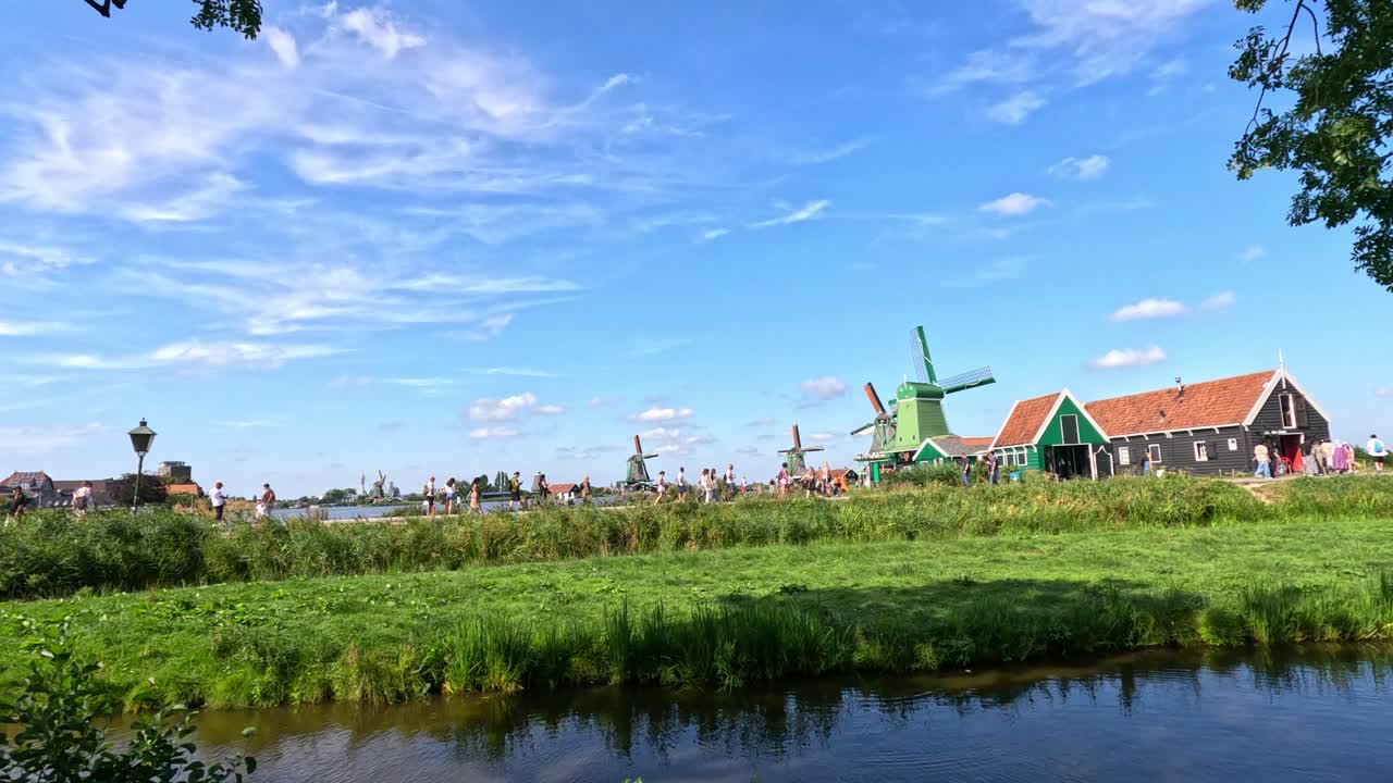 Wide shot of windmills, canal, and green fields under bright daylight with gentle camera pan