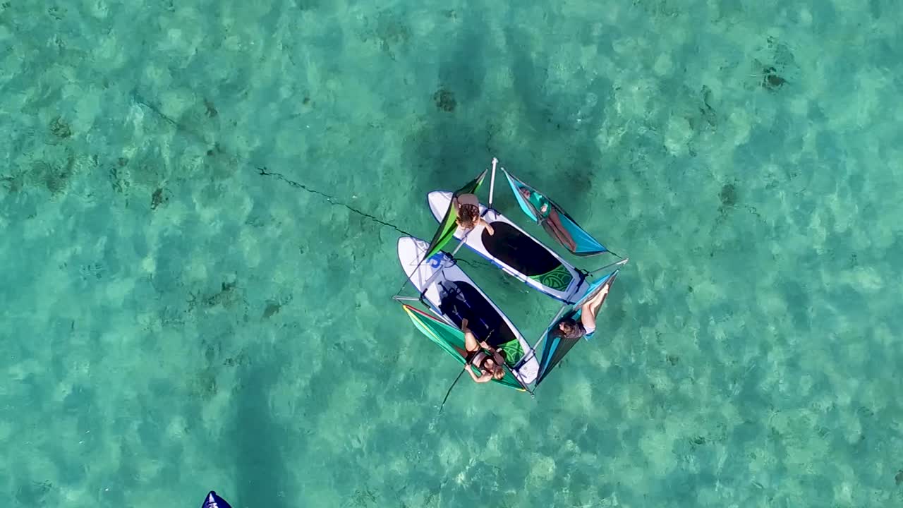 Aerial top-down view of people in hammocks on wakeboards, couple kayaking in clear blue water
