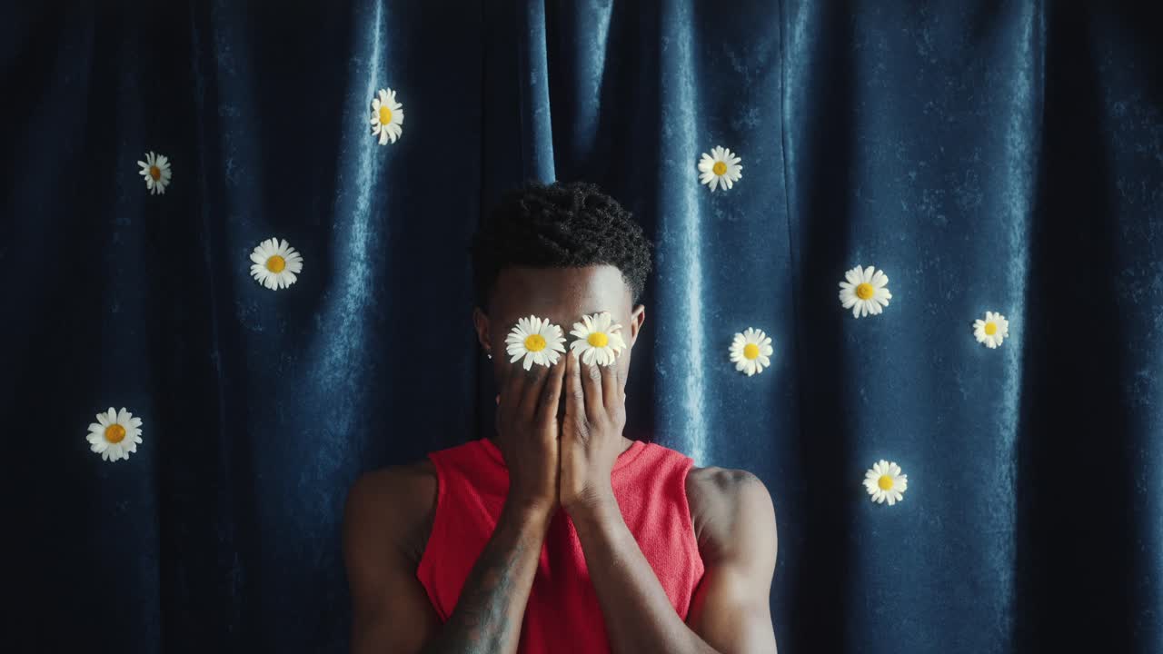 Man Covering Face With Hands Holding Daisies against Blue Curtain