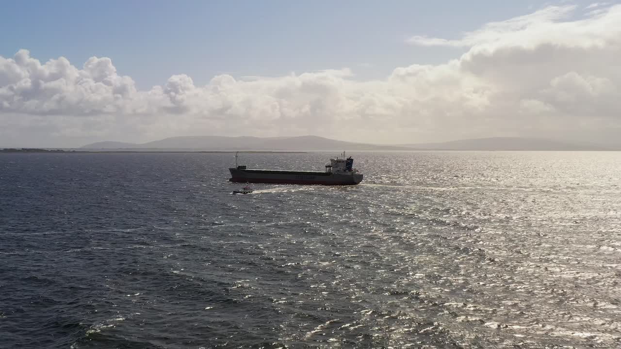 visión general de un avión no tripulado de ángulo alto de un barco piloto guiando un gran buque cisterna cerca de la isla de mutton en la bahía de galway, rodeado por el vasto océano y la atmósfera serena