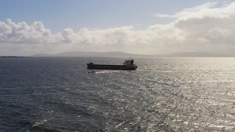 high-angle drone overview of a pilot boat guiding large tanker ship near mutton island in galway bay, surrounded by the vast ocean and serene atmosphere