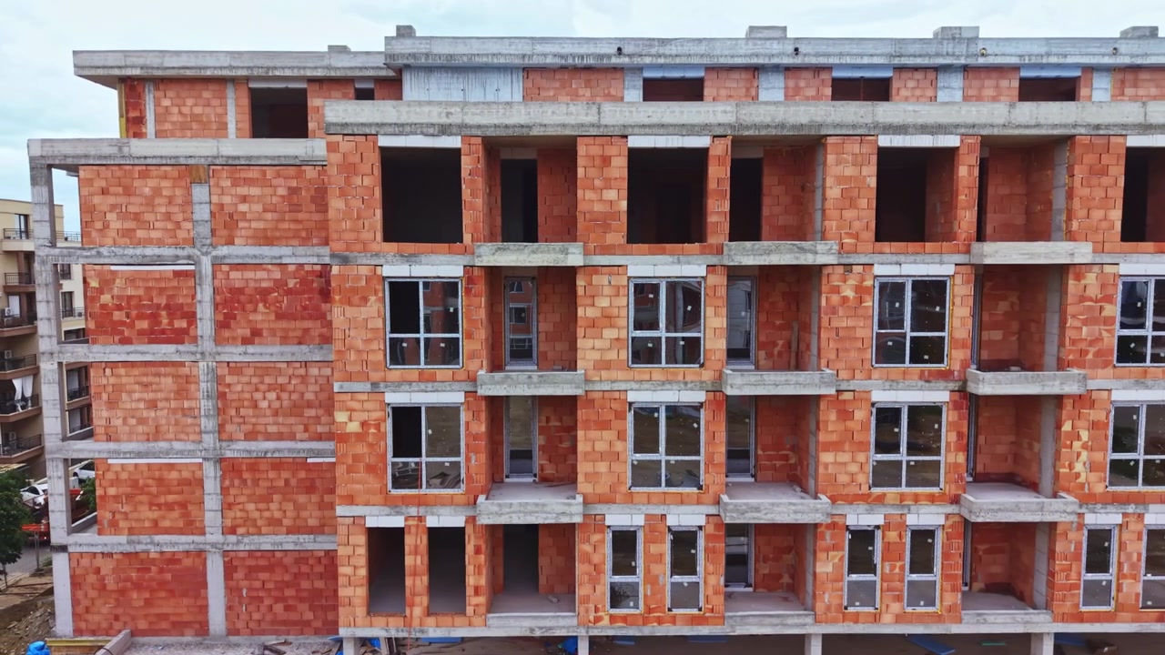 Ufærdig boligstruktur, der fremviser rå murstens- og betondetaljer. En ufuldstændig facade på et lejlighedskompleks, der afslører rødt murværk og industrielle arkitektoniske træk.