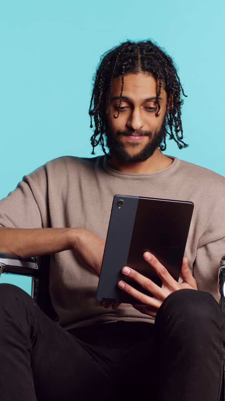 Vertical video Man in wheelchair chatting with friend over internet videocall using tablet