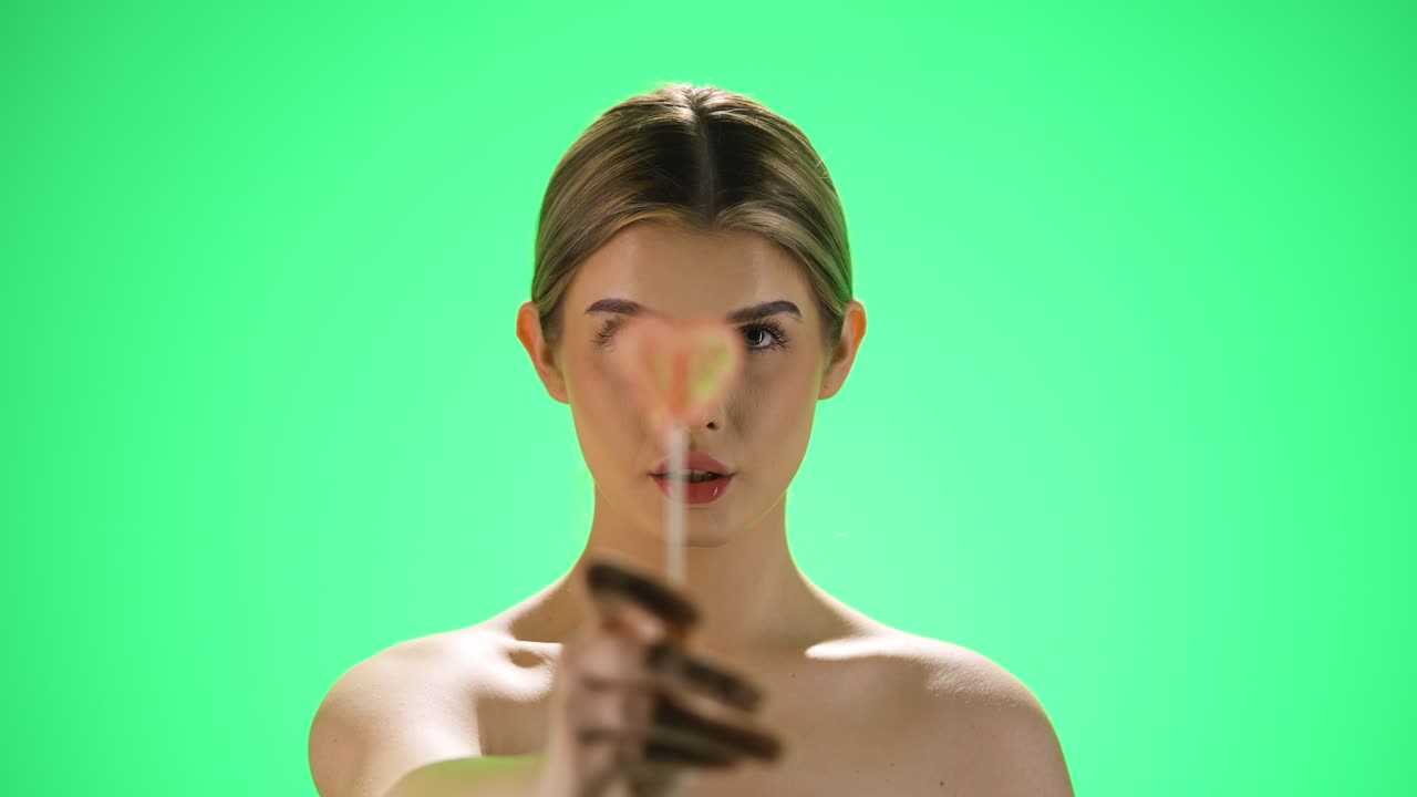 녹색 배경 에 사탕 을 보여 주는 카메라 에 심장 모양 의 맛있는 달 ⁇ 한 롤리 나 롤리팝 을 들고 있는 젊은 예쁜 금발 여자 의 정적  ⁇