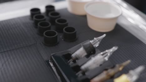 various tattoo needles and ink being prepared on table by tattoo artist before inking session, ink cups being filled with black drops