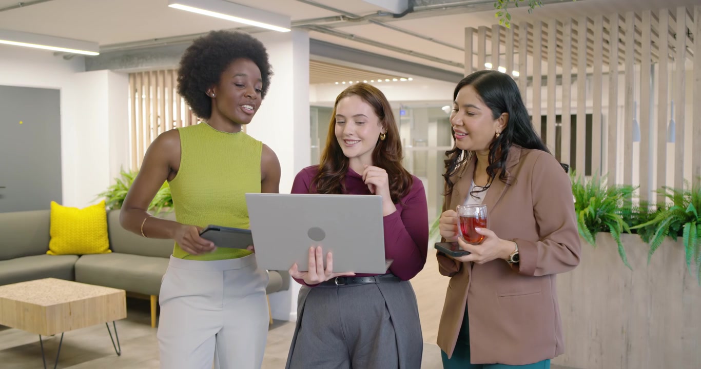 Diverse vrouwelijke collega's vergaderen in een loungeruimte, tonen een laptop en gebruiken een tablet voor feedback.
