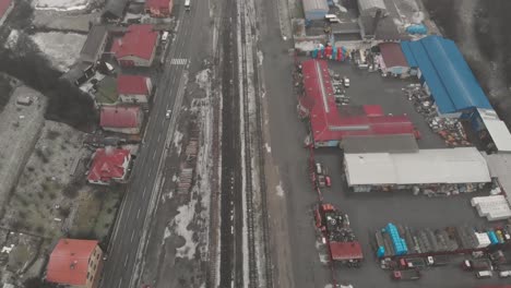 Tiro-De-Seguimiento-Aéreo-Sobre-El-área-Industrial-De-Invierno-Con-Tráfico,-Ferrocarriles-Y-Almacenes