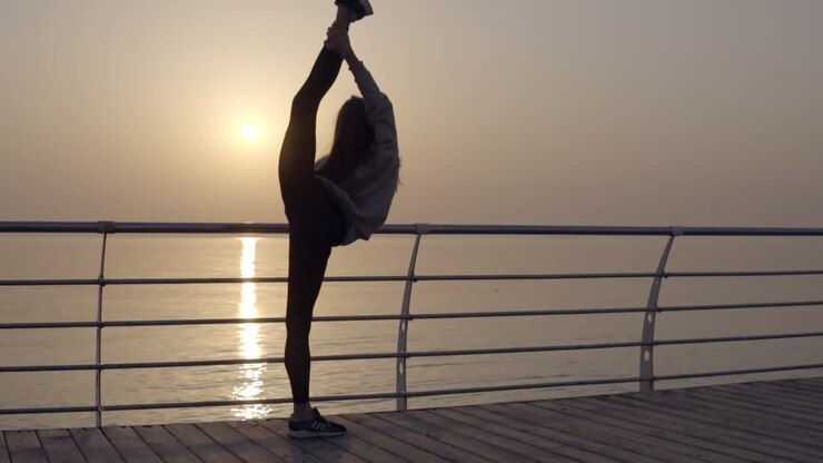Long haired girl stretches her leg with a view of the sea ocean. Dawn Sunrise. Sportswear, leggings, hoodies. Dusk