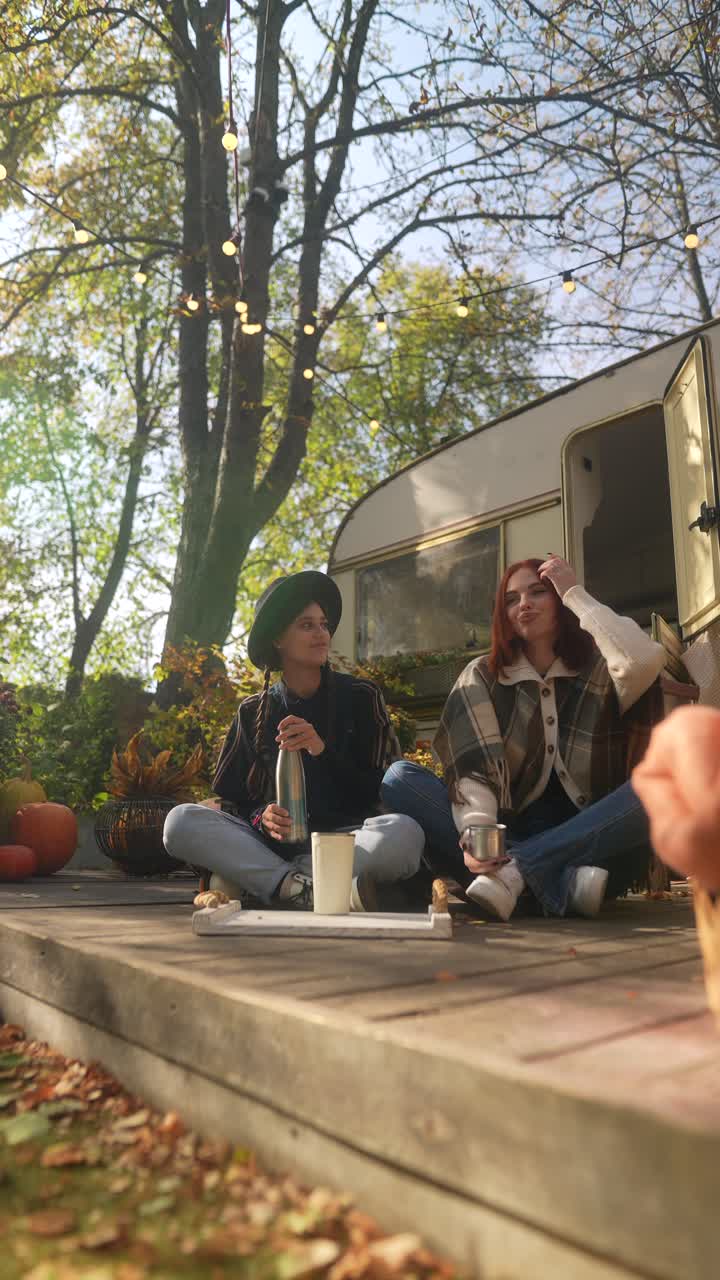 두 친구 가 가을 에 야외 의 나무 갑판 에서 음료 를 즐기고 있다