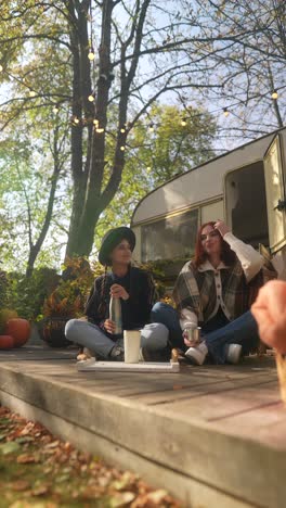 two friends enjoying drinks on a wooden deck outdoors in autumn