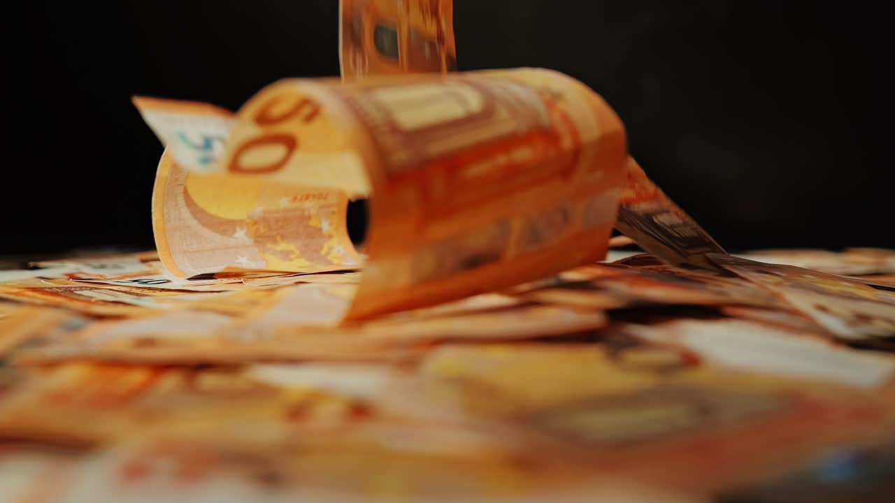 Banconote di euro cinematografiche svolazzano e atterrano dolcemente durante una ripresa statica ad alto contrasto.