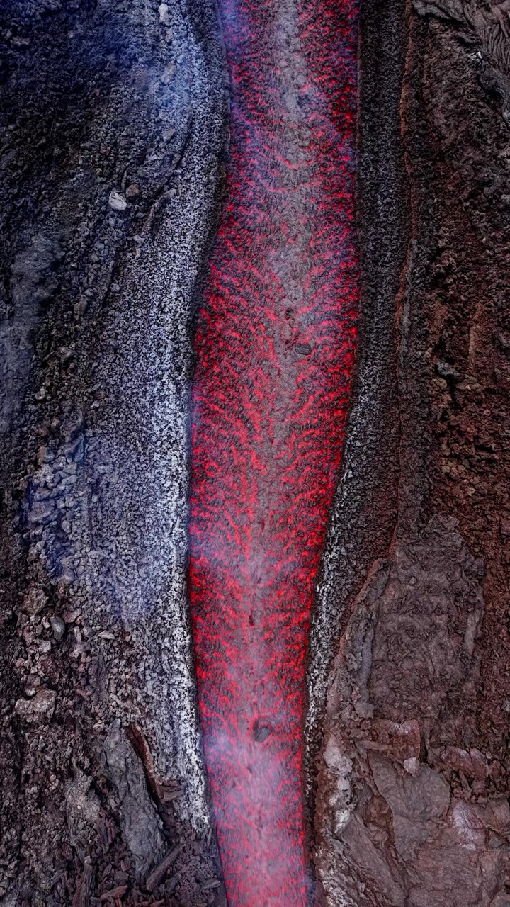 Vista aerea di un fiume di lava incandescente e terreno vulcanico con fumo che si innalza dall'Etna.