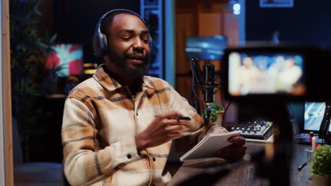 man recording interview with professional camera in studio, reviewing notes to ask questions