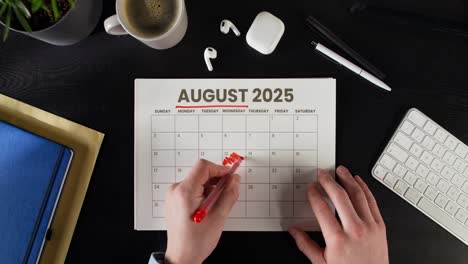 person marking dates on august 2025 calendar