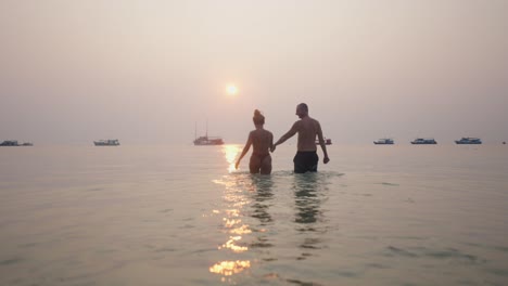 romantic couple walking hand-in-hand in the ocean at sunset