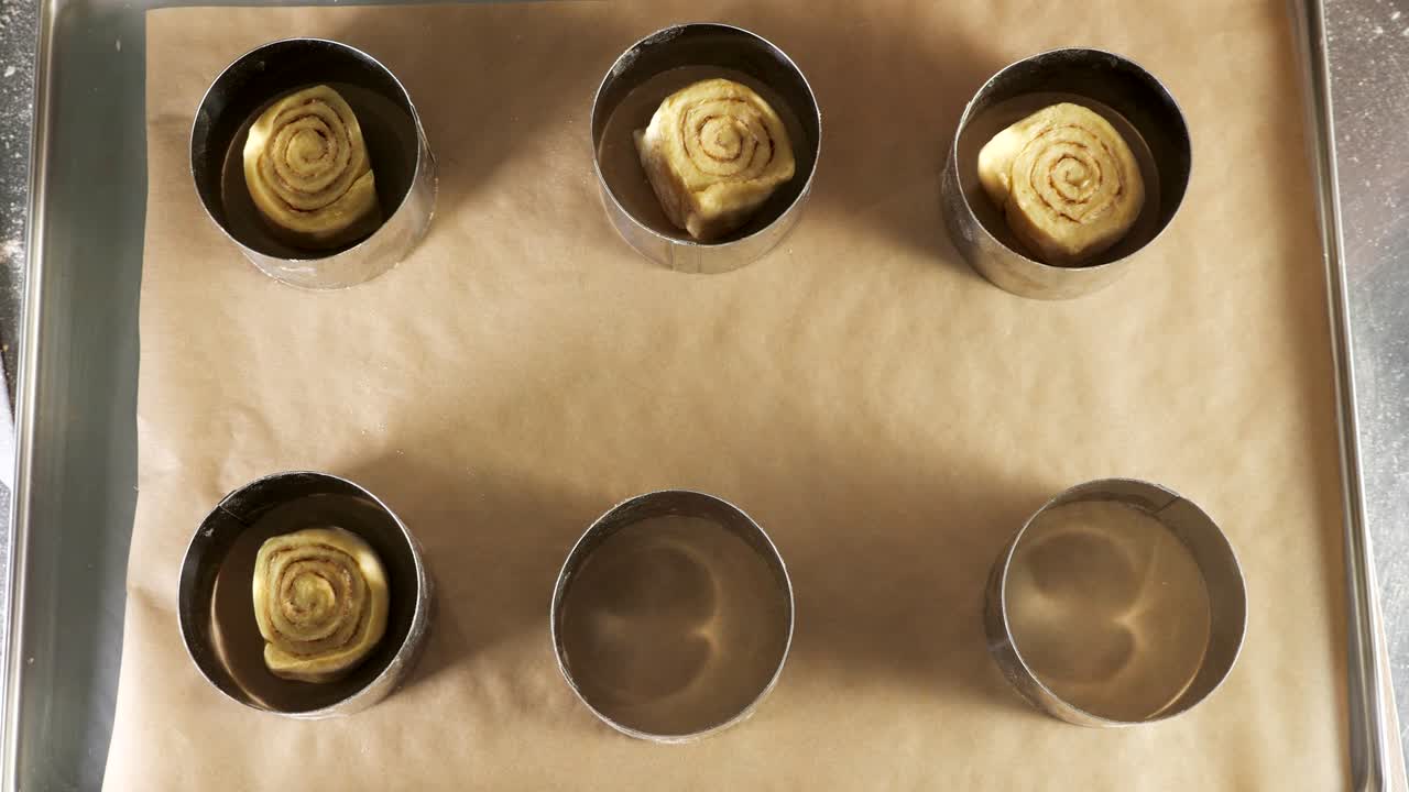 베이커는 카네몬 롤을 기 위해 양식을 채우는 롤을 위해 반죽을 넣습니다.