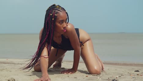 a young girl in a bikini at a vibrant caribbean shore kneel in the sand with ocean waves in the background