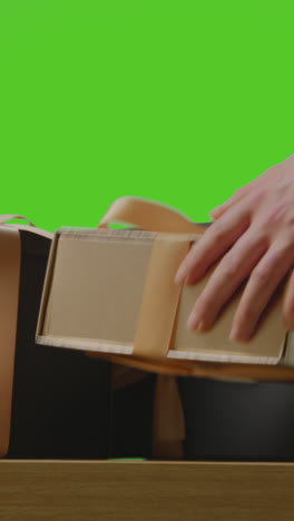 video vertical de un hombre recogiendo un regalo en una caja envuelta decorado con cinta en la mesa disparado contra la pantalla verde 2