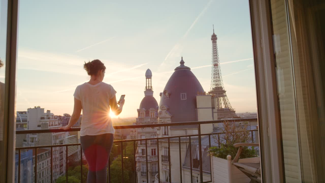 Filmato video 4K di una giovane donna in piedi sul balcone del suo appartamento a Parigi che usa il suo smartphone.