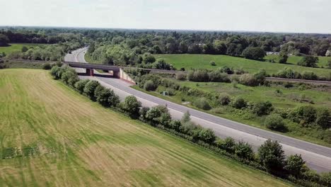 drone flying over a34 trunk road which is intersected by a railway bridge crossing, showing transport cutting through countryside in the uk