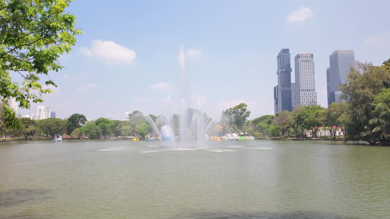 Bangkoks skyline og skyskrabere spejlet i Lumphini Parks sø og springvand.